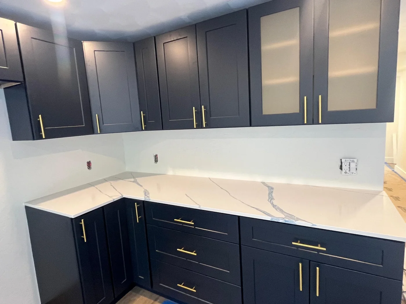 Navy shaker kitchen cabinets with gold pulls and a white stone countertop