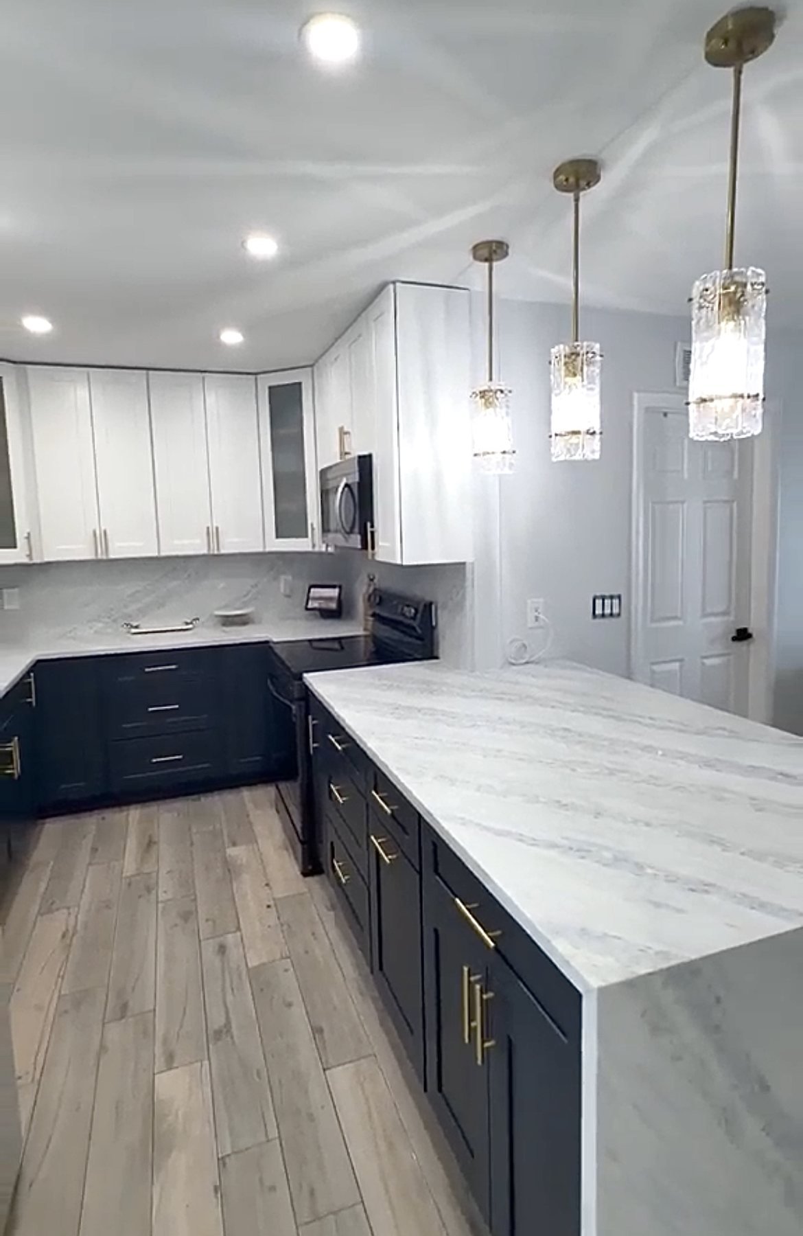 After: white upper cabinets over navy lowers, a marble waterfall island and crystal pendants