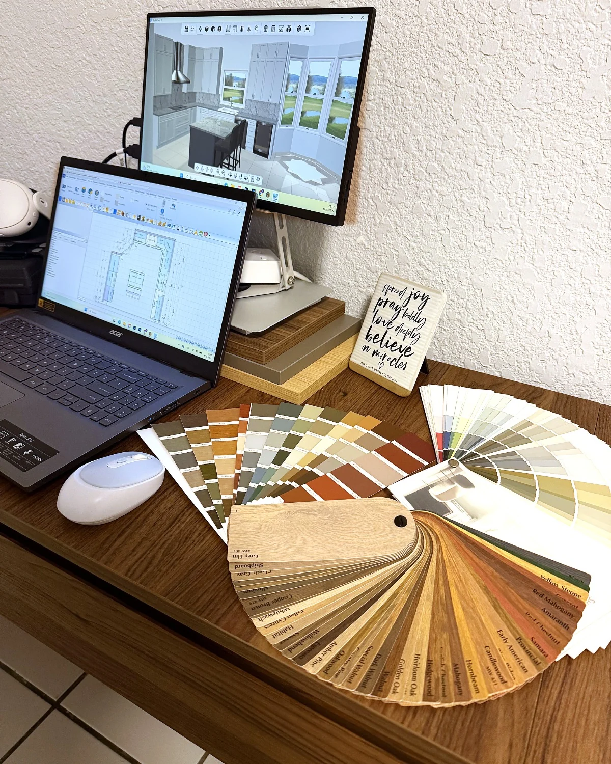 Desk with a laptop showing the floor plan and a monitor showing the 3D kitchen, next to door and finish samples